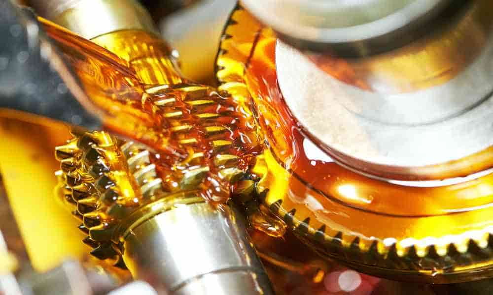 Thick, honey-colored lubricant is poured onto clean metal gears. The lubricant spreads across the components and drips down.