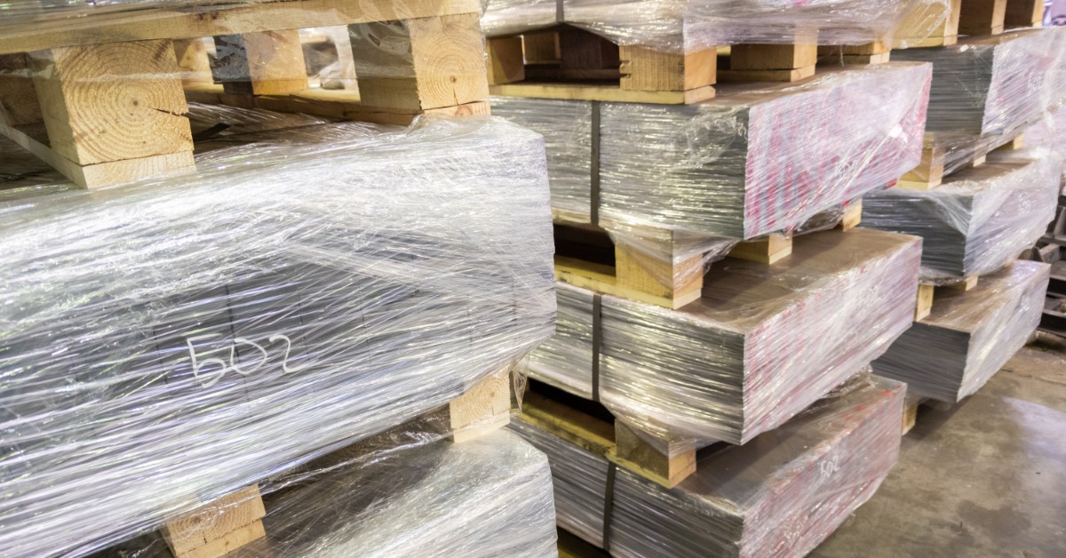Stacks of plastic-wrapped materials rest on wooden pallets over a gray concrete floor in an indoor storage area.