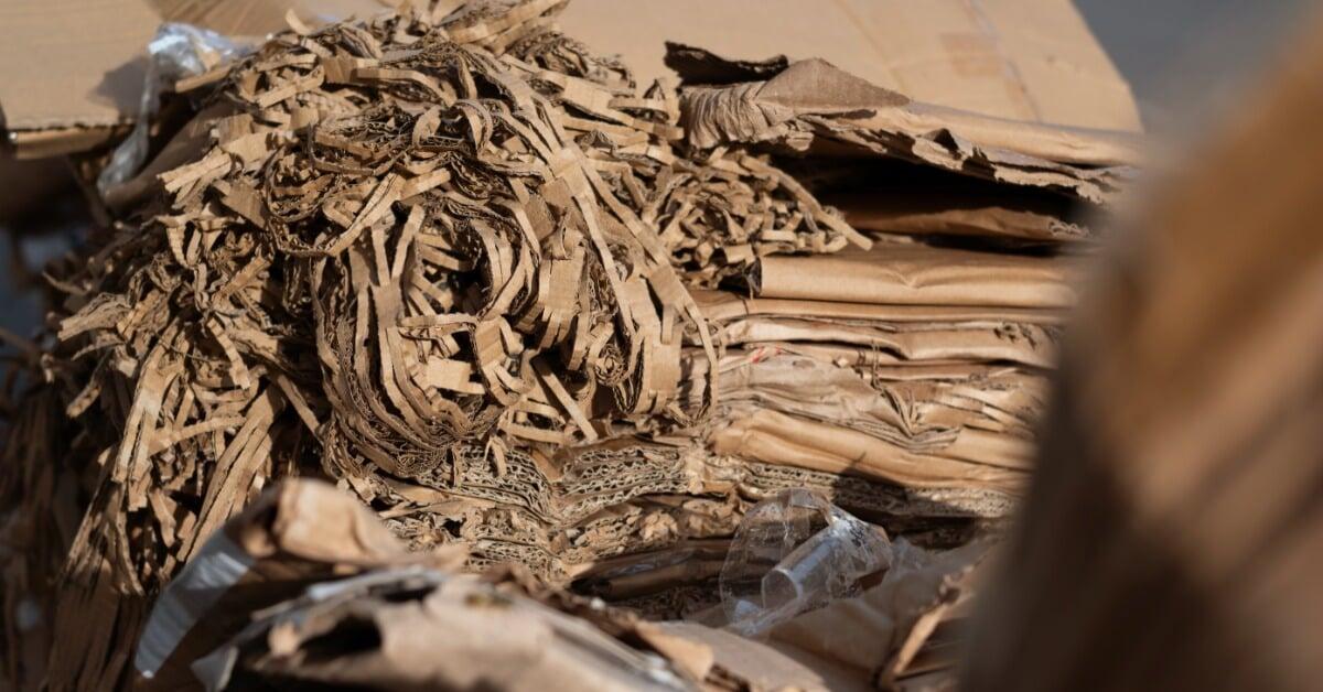 Shredded corrugated cardboard strips and flattened boxes form a brown pile with torn edges and layered pieces.