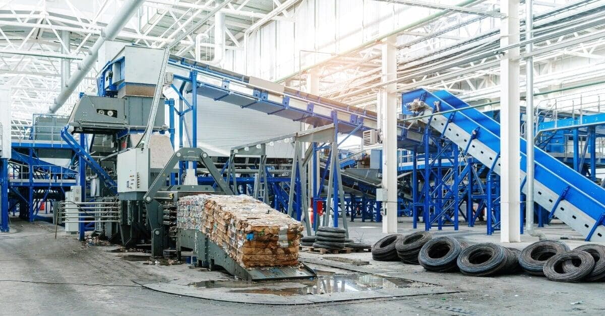 Blue conveyor systems and recycling machinery surrounding a compressed cardboard bale with ties lying on the floor.