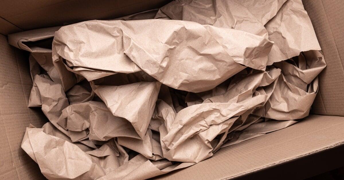 A close-up of an open cardboard box containing crumpled brown packing paper folded into layers to cushion a product.