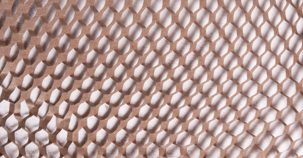 An extreme close-up of light brown honeycomb paper packaging filler stretched across a white surface.