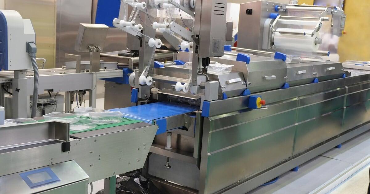 A stainless steel food packing equipment with blue conveyor belts and plastic film rolls in a clean, industrial setting.
