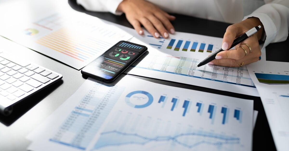 A person analyzing business data with a pen, reviewing charts and graphs on documents set on a desk.