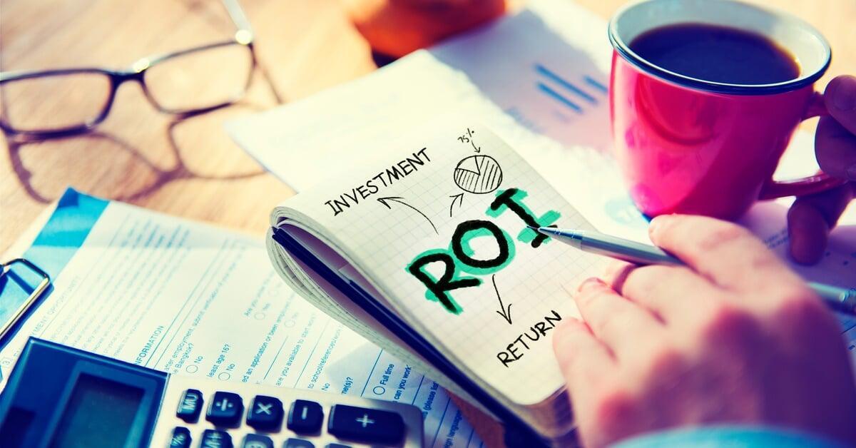 A hand holding a pen, pointing at a notebook with 'ROI' and 'Investment' written on it, alongside a pie chart labeled '35 percent.'