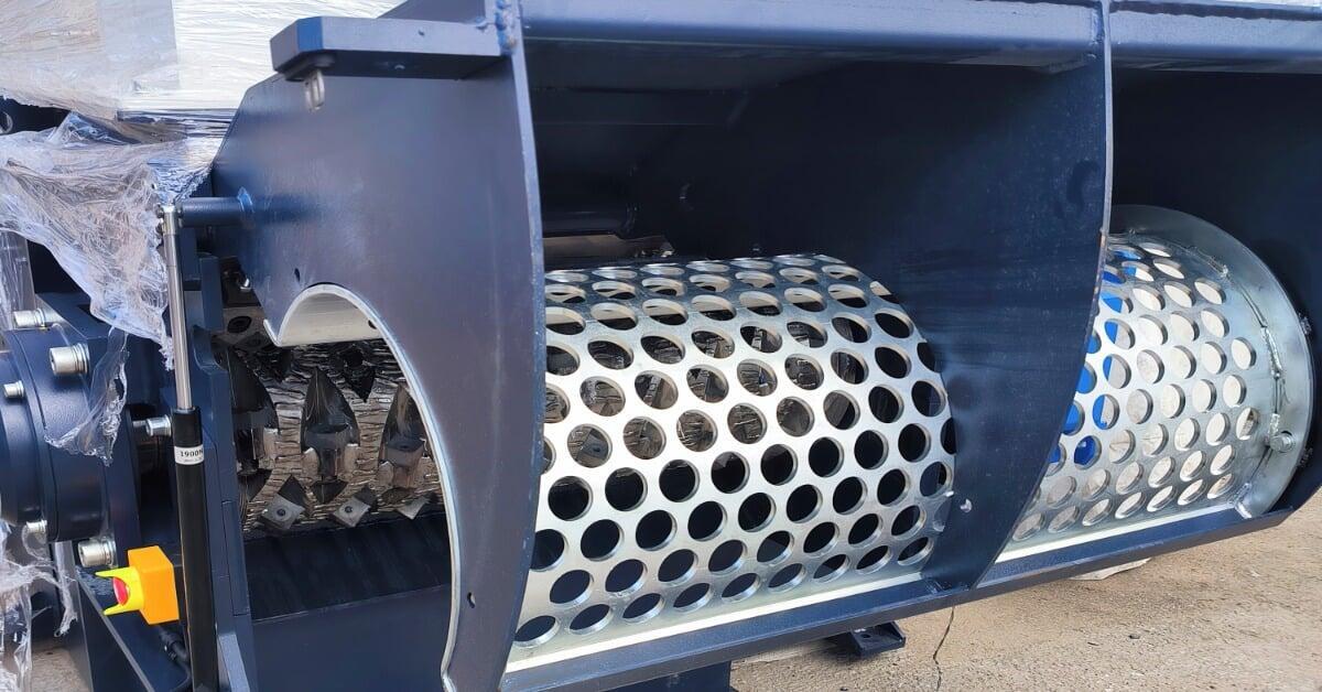 A single-shaft mechanical industrial shredder with visible gears and a cylindrical component with circular holes.
