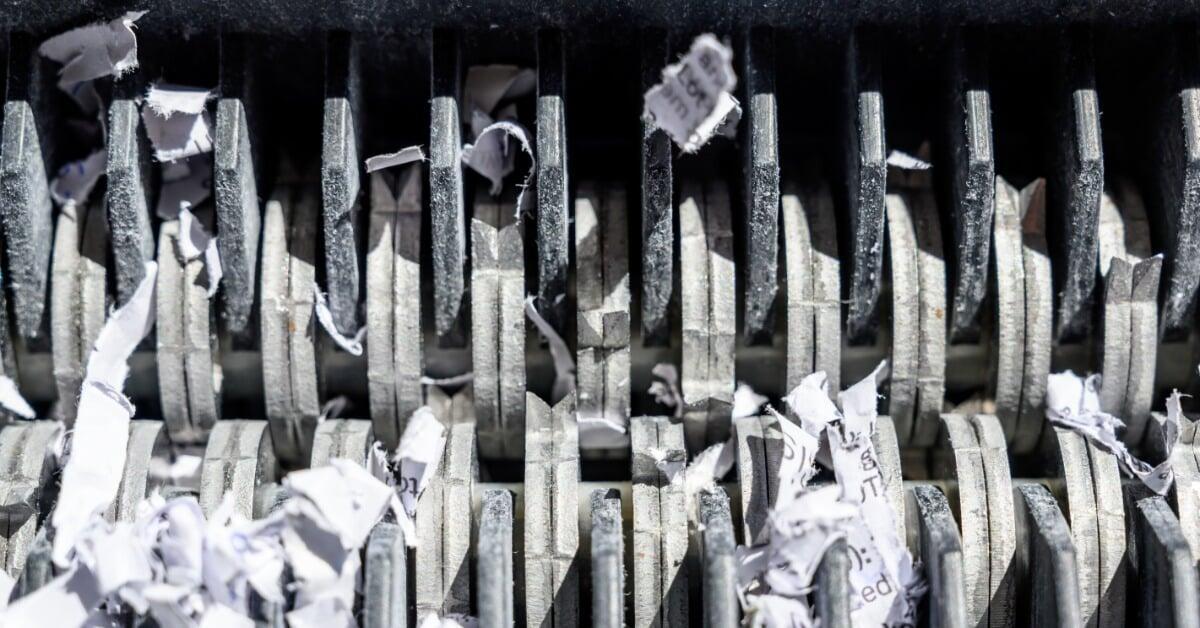 A close-up view of a paper shredding machine’s teeth with shredded paper intertwined inside of its blades.