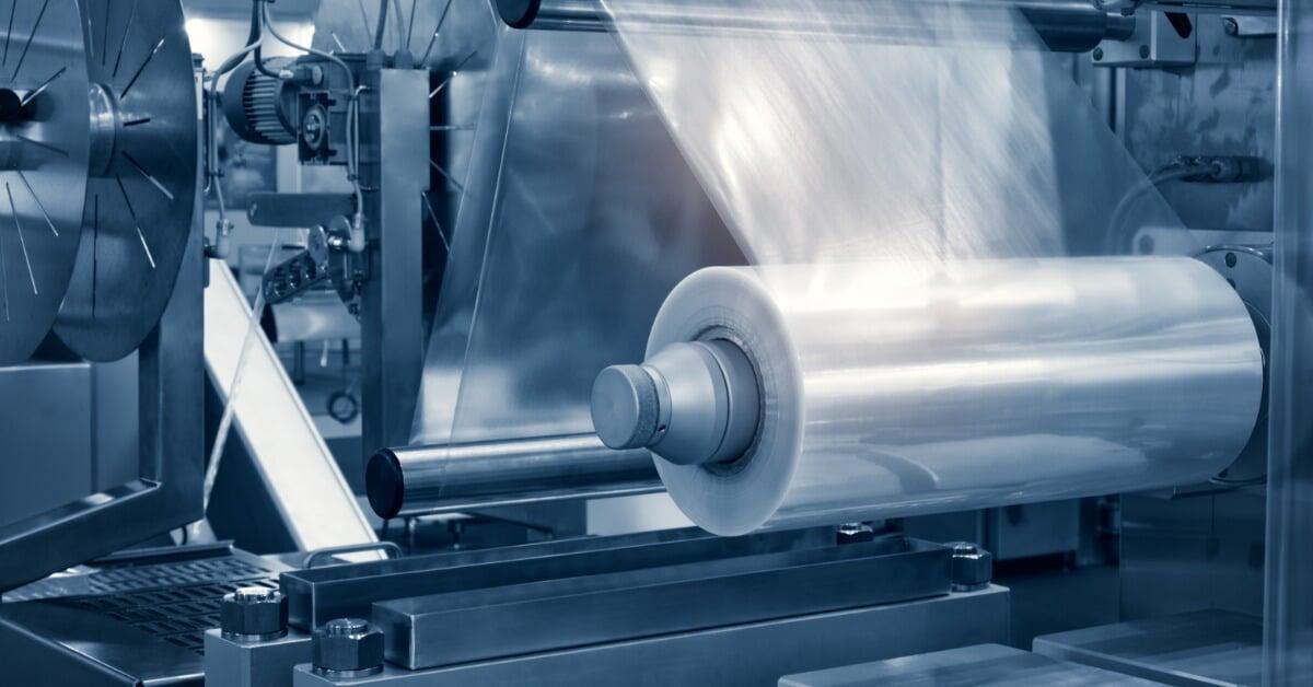 An automatic plastic bag production machine operates with a large roll of transparent plastic film fed through rollers.