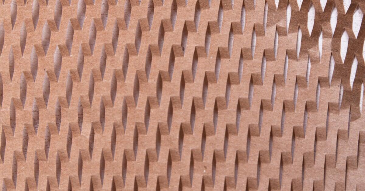 A close-up of brown paper packaging filler shows a repeating honeycomb pattern over a white background.