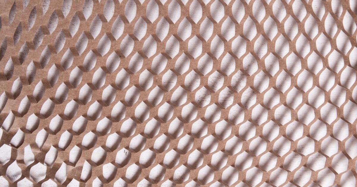 Strips of crimped white packing paper sit inside an open brown shipping box on top of a brown background.