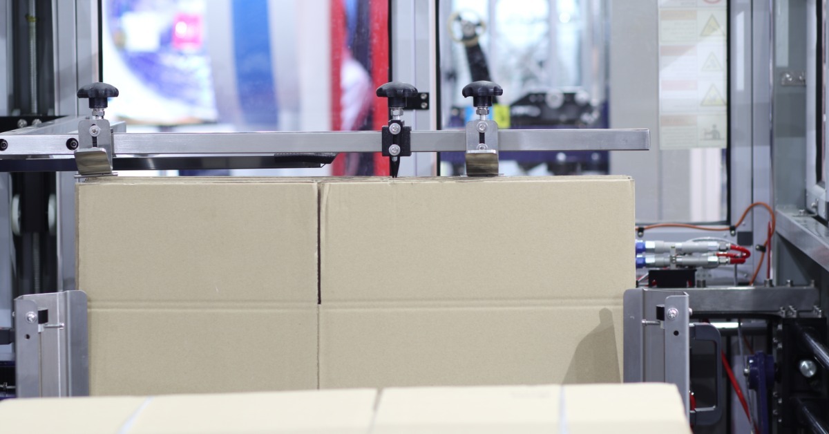 A carton box erector machine holding a single cardboard box within its metal frame and mechanical components.