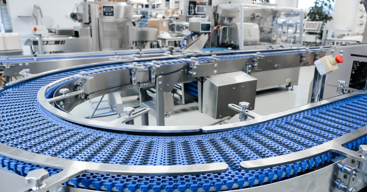 A large, curved blue conveyor belt runs through stainless steel equipment on a modern factory production line.