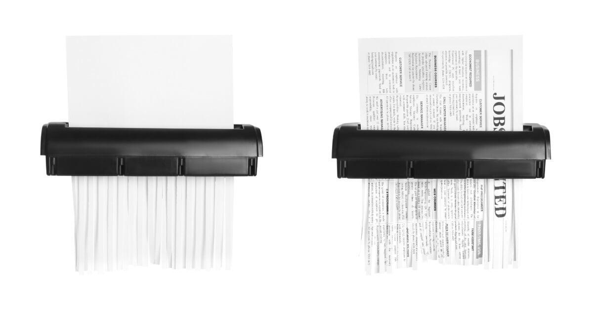 Two office paper shredders feed sheets through cutting blades, turning documents into thin strips on a white background.