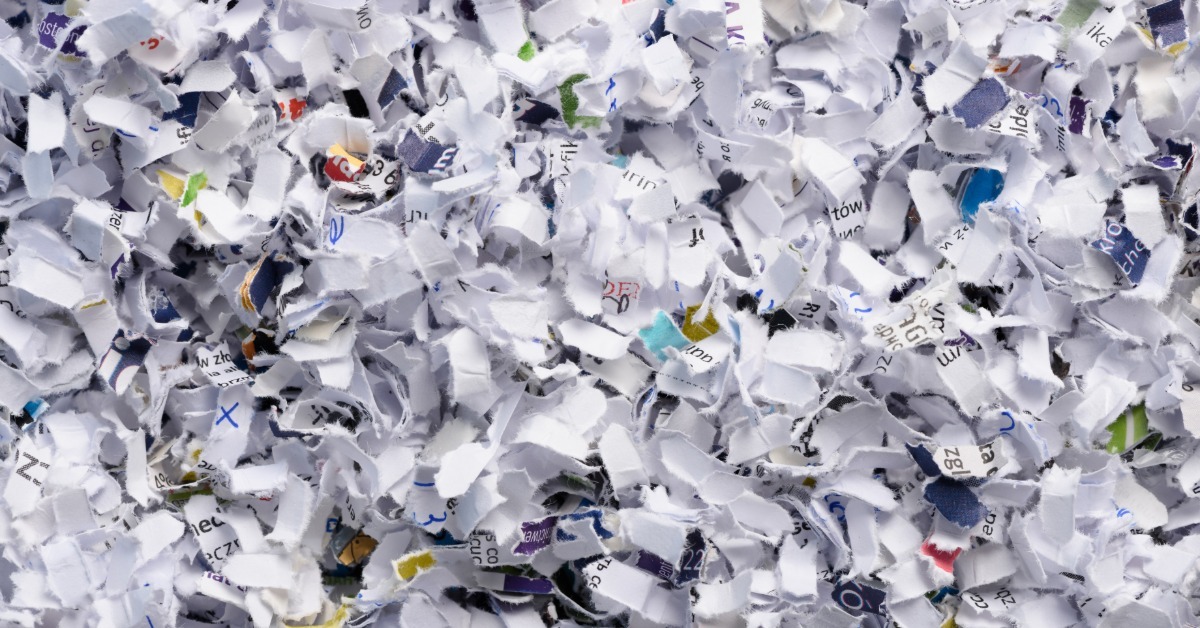 A pile of cross-cut shredded paper pieces forming a textured background made of white and printed document fragments.