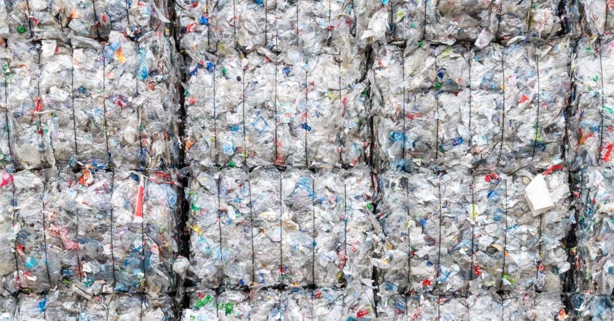 Several stacks of tightly compressed plastic waste form large cube bales, arranged in rows and bound with visible wires.