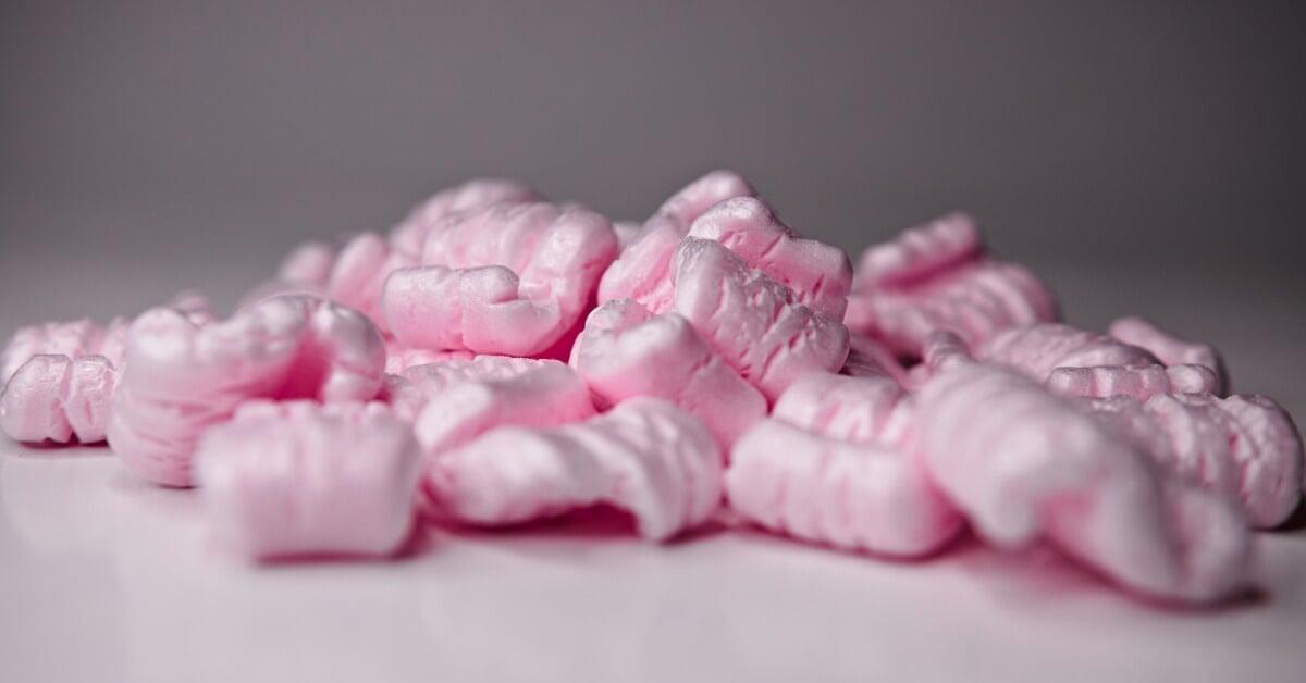 Several irregularly shaped pieces of pink packing foam sit in a loose pile on a flat, white surface.