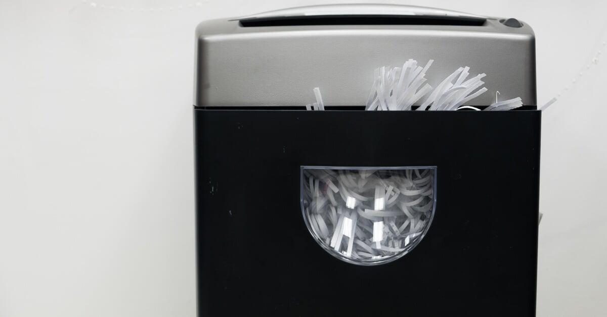 A gray and black document shredder holding sheets of white paper against a plain white background with no other objects.