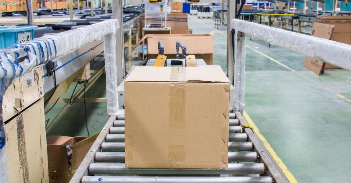 A yellow strapping machine spanning roller conveyors as cardboard boxes move through an industrial packaging line.