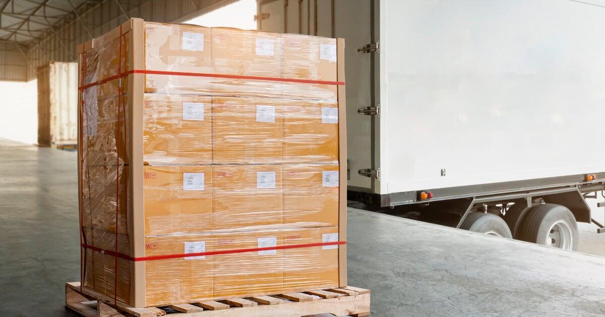 A wrapped and strapped pallet of goods sitting on a loading dock. The pallet is near the back of a freight truck.