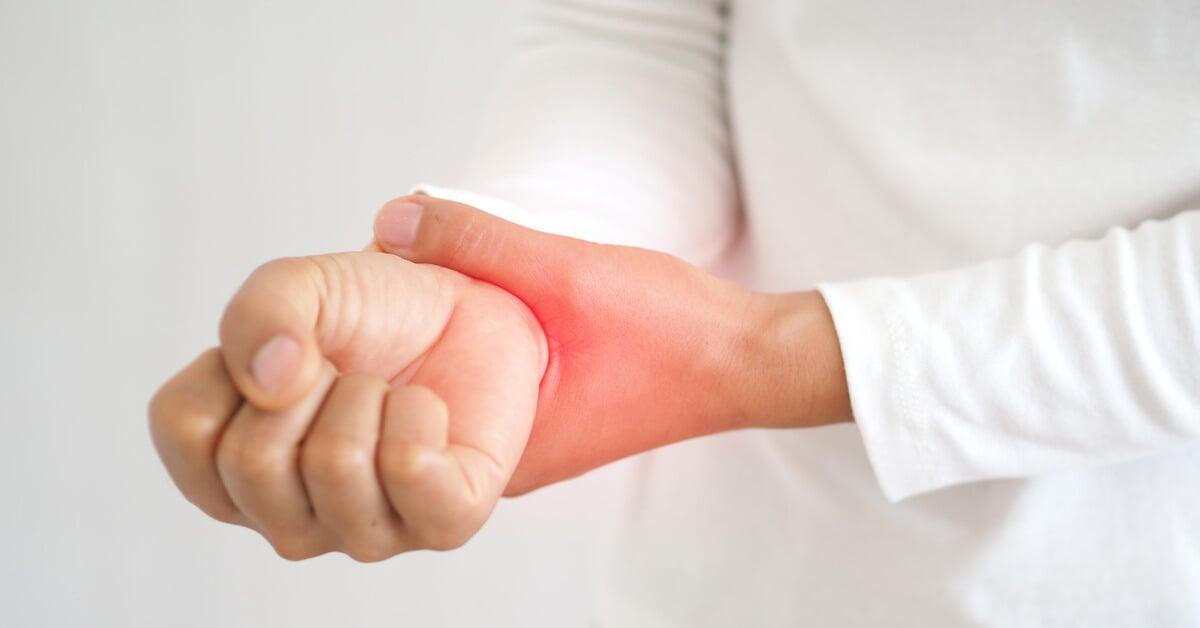 A person wearing a long-sleeved white shirt holds their right wrist. Their hand is in a fist it glows red.