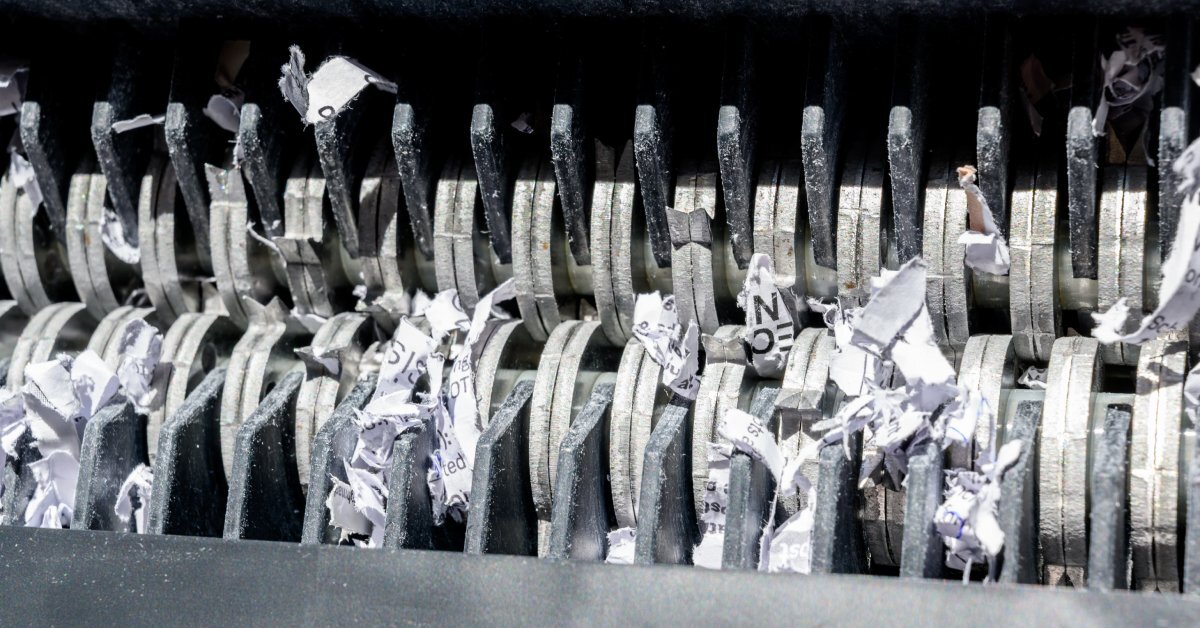 A close-up view of the metal teeth on a black shredding machine. Shreds of white paper are between some of the teeth.