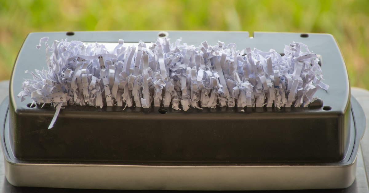 The top of a paper shredding machine with a dark lid. The opening is full of a thick wad of shredded paper.