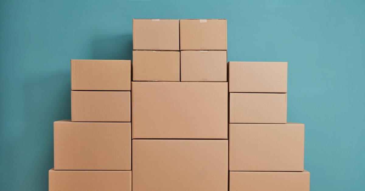 Cardboard boxes of different sizes are neatly stacked against a teal wall. The cases have no writing or labels on them.