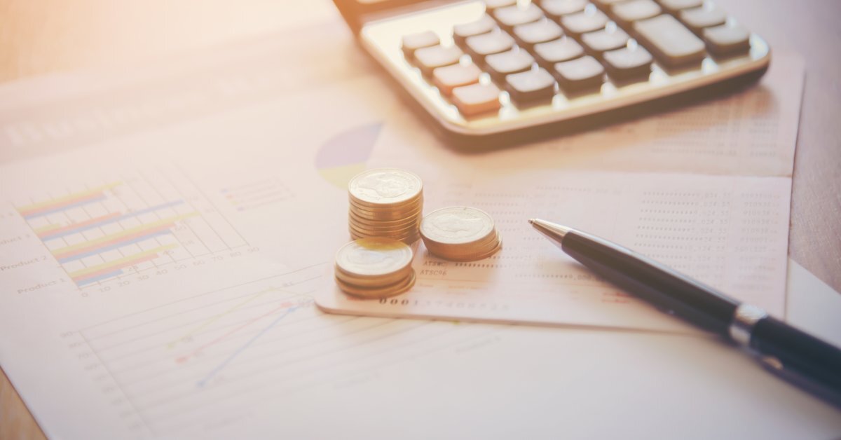 A calculator, pen, and coins on top of sheets of paper. One sheet shows a bar graph, a line graph, and part of a pie graph.