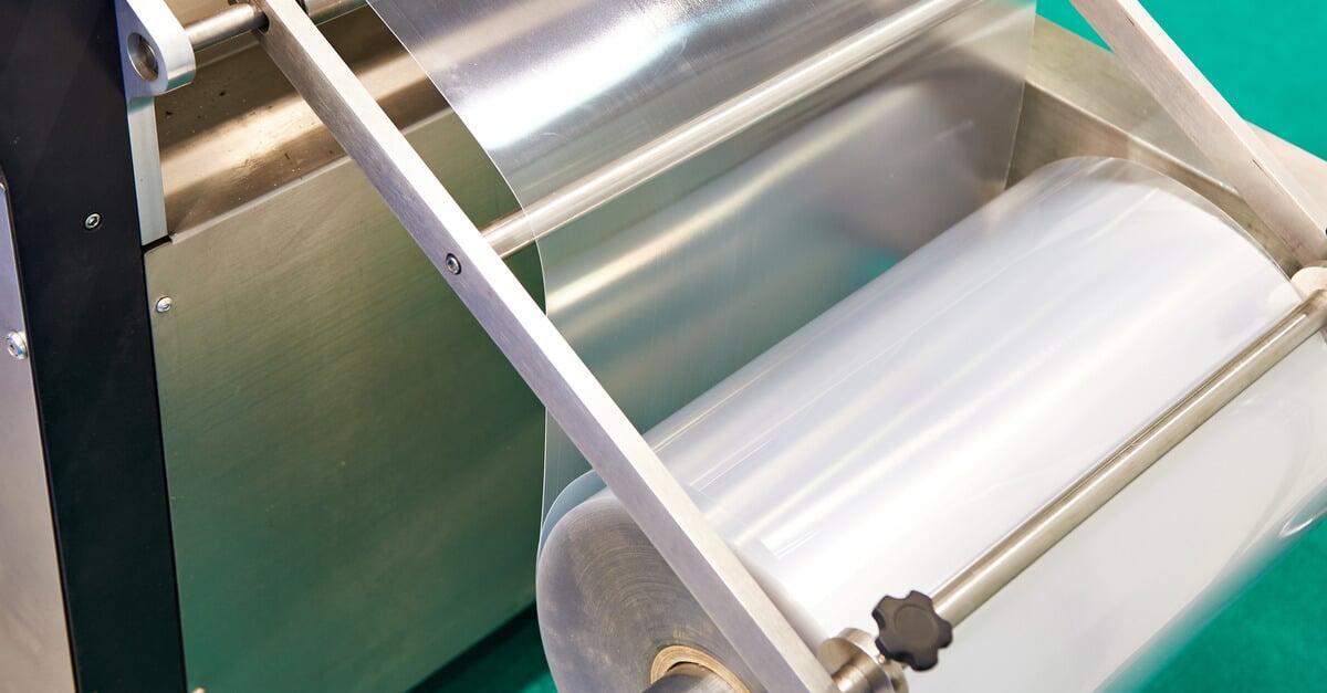 A dispenser attached to a machine holds a roll of stretch film horizontally. One end of the film is in the machine.