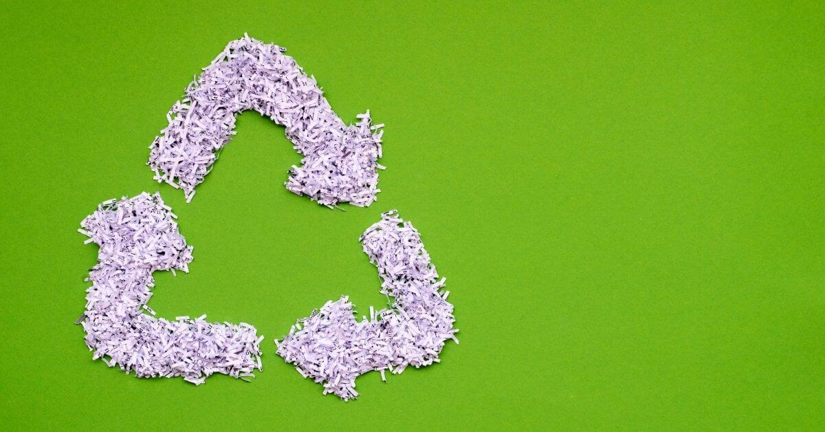 Shredded paper arranged into the shape of the three-arrow recycling symbol. The paper lies over a green background.