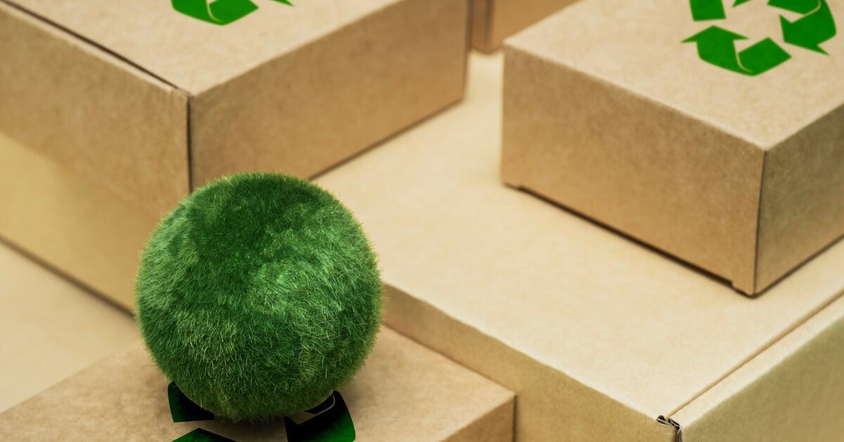 Several cardboard boxes neatly piled together. The recycling symbol is printed on the boxes and a grassy ball sits on one box.