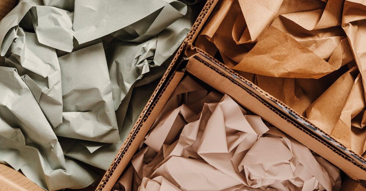 An overhead view of three open cardboard boxes containing paper void fill. The paper is colored off-white, brown, and gray.