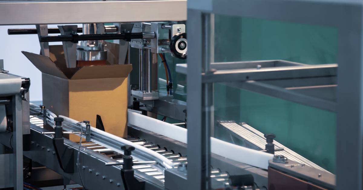 A machine holding a cardboard case open on a roller conveyor. Bars on either side of the conveyor keep the box sides straight.