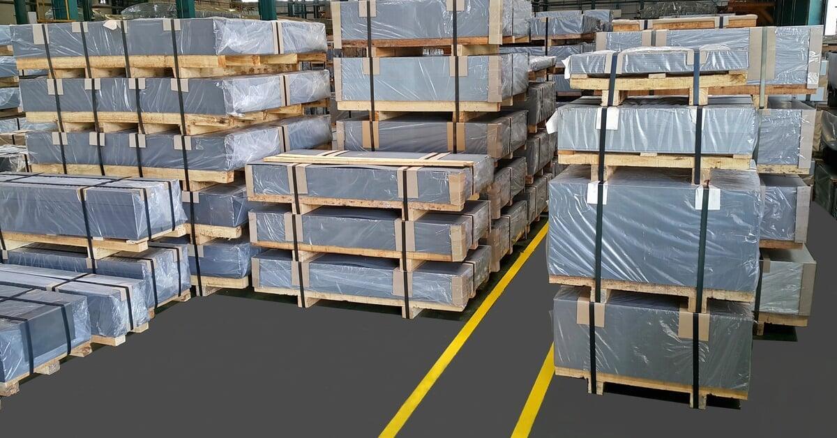 A warehouse full of stacked goods wrapped in plastic and sitting on wooden pallets secured with black straps.