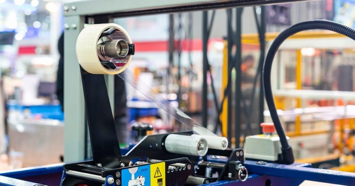 A close-up of a roll of clear masking tape on a tape dispenser that is part of an automatic sealing machine.