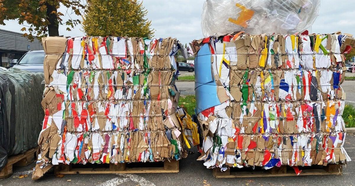 Two large trash bales secured with ties sitting on wooden pallets outside. One bale has a clear bag of trash on top.