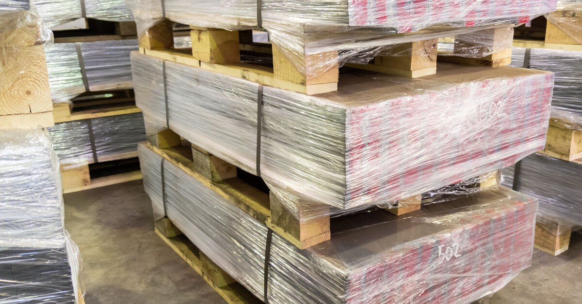 Stacks of palletized goods set up on a concrete floor. The items are secured with clear stretch wrap and straps.