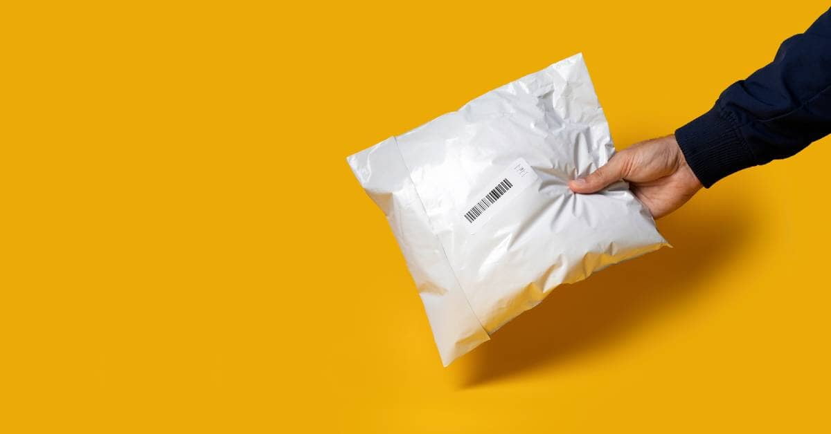 A person outside of the frame holding out a white, sealed polyethylene bag over a yellow background. The bag has a barcode.