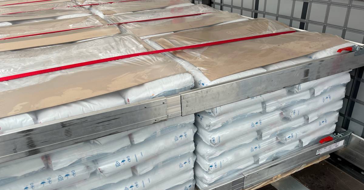 Bulk materials in bags stacked on pallets. The palletized goods are in a semi-trailer, and red strapping keeps them in place.