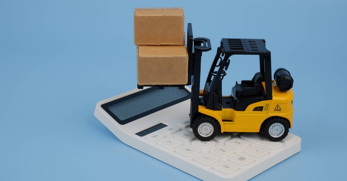 A miniature yellow lift truck on top of a white calculator. The lift truck's raised forks carry two unlabeled cardboard boxes.