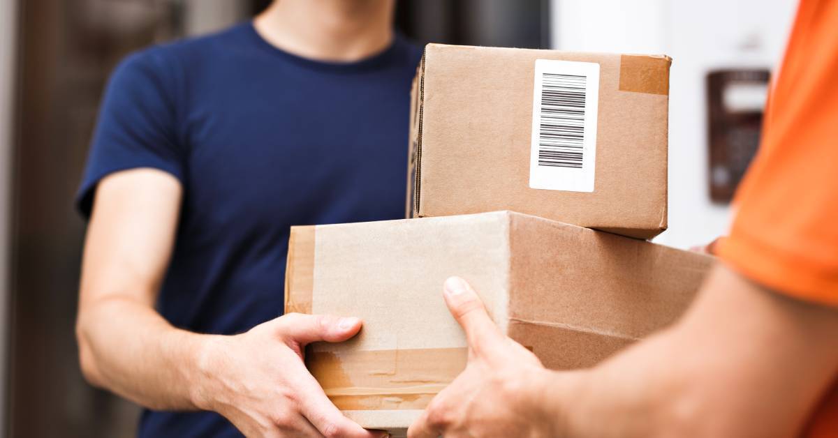 A person in an orange shirt handing two stacked packages to someone in a blue shirt. The cardboard boxes are in good condition.